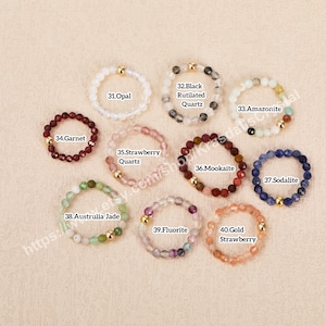 Peut inclure: Dix bracelets en pierres pr&eacute;cieuses avec des perles dor&eacute;es. Chaque bracelet est fait avec un type de pierre pr&eacute;cieuse diff&eacute;rent, y compris l'opale, le grenat, le quartz fraise, le quartz rutil&eacute; noir, l'amazonite, la mookaite, la sodalite, le jade d'Australie, la fluorine et la fraise dor&eacute;e.