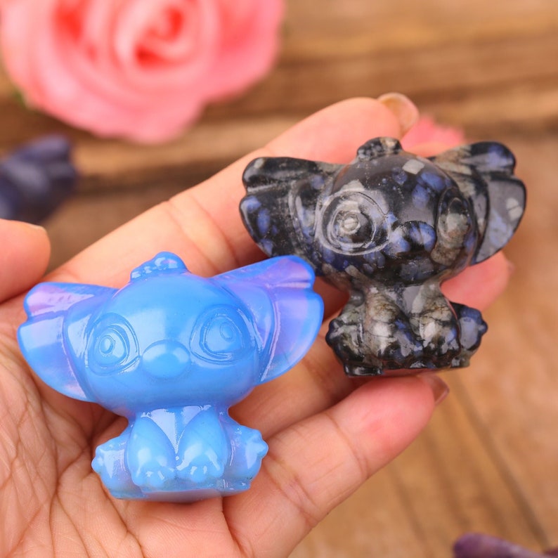 Op de afbeelding: Twee kleine, handgesneden kristallen beeldjes van Stitch, een cartoonfiguur uit de Disney-film Lilo & Stitch. E&eacute;n beeldje is blauw en het andere is zwart.