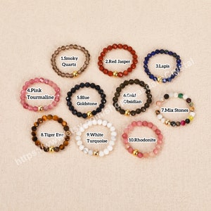 Peut inclure: Dix bracelets en pierres pr&eacute;cieuses avec des perles dor&eacute;es. Les bracelets sont dispos&eacute;s en cercle sur un fond beige. Les pierres pr&eacute;cieuses comprennent le quartz fum&eacute;, le jaspe rouge, le lapis-lazuli, la tourmaline rose, la goldstone bleue, l'obsidienne dor&eacute;e, des pierres m&eacute;lang&eacute;es, l'&oelig;il de tigre, la turquoise blanche et la rhodonite.