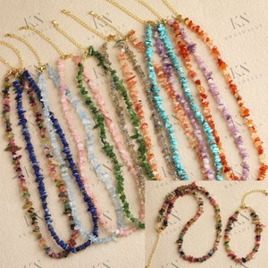 May include: A set of ten delicate gold chain necklaces with various gemstone chips. Each necklace features a different colour combination of chips, including pink, blue, green, red, and purple. The necklaces are displayed on a light beige surface.