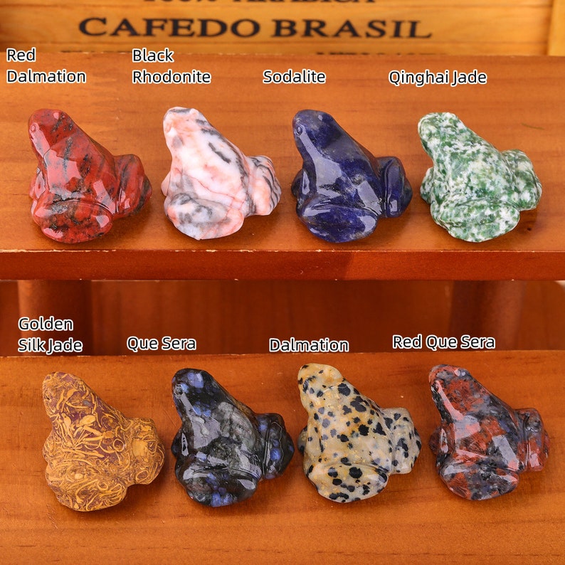 K&ouml;nnte beinhalten: Zehn kleine Froschfiguren, die aus verschiedenen Steinsorten geschnitzt sind. Die Fr&ouml;sche sind in zwei Reihen zu f&uuml;nf angeordnet. Die Steine umfassen roten Dalmatiner, schwarzen Rhodonit, Sodalith, Qinghai-Jade, goldene Seidenjade, Que Sera, Dalmatiner und roten Que Sera.
