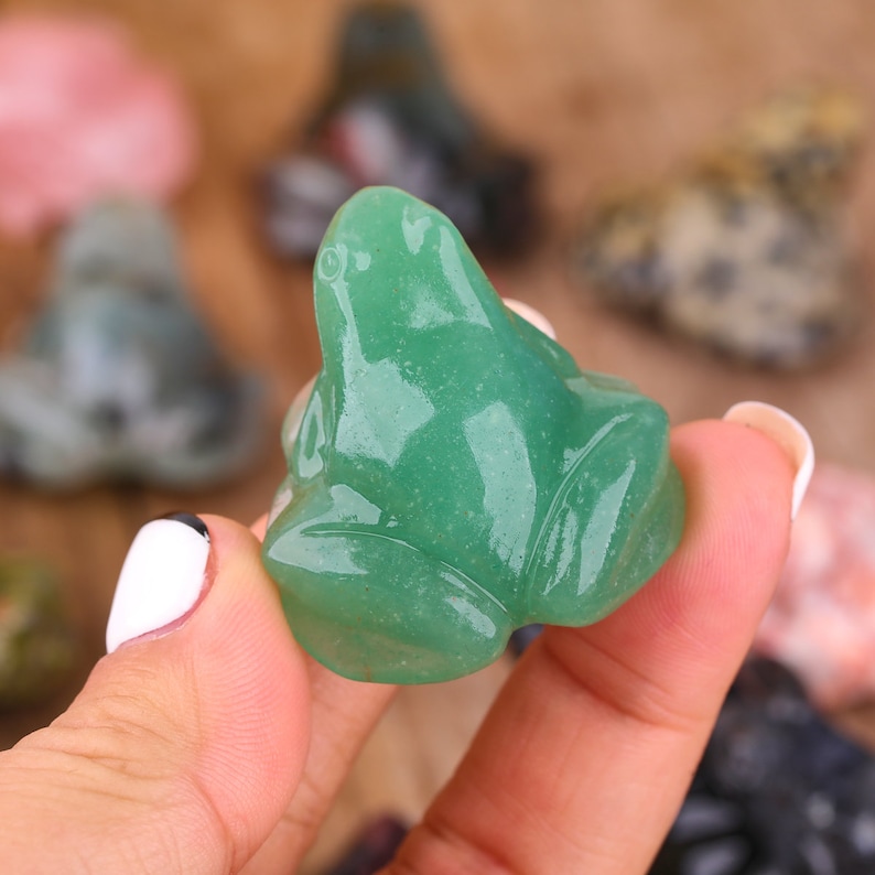 K&ouml;nnte beinhalten: Eine gr&uuml;ne Jade-Froschfigur. Der Frosch sitzt mit ausgestreckten Beinen und leicht nach oben geneigtem Kopf. Die Figur ist glatt und poliert, mit einem leichten Glanz.