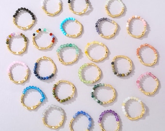 Peut inclure: Une collection de vingt-deux bagues, chacune composée d'un anneau en métal doré à la texture irrégulière, partiellement orné d'une rangée de petites perles de pierres précieuses rondes et colorées, incluant des tons bleus, verts, roses et noirs.