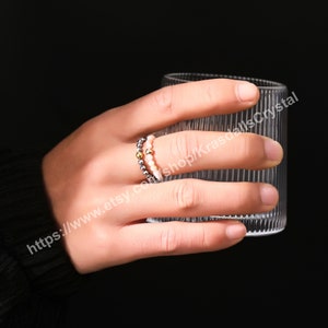 Peut inclure: Une main portant deux bagues en perles. Les bagues sont faites de petites perles rondes dans des tons de rose, d'or et d'argent. Les bagues sont empil&eacute;es l'une sur l'autre.