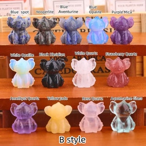 Op de afbeelding: Twaalf kleine, gegraveerde kristalfiguren van Stitch uit de Disney-film Lilo & Stitch. De figuren zijn gemaakt van verschillende soorten kristallen, waaronder blauwe aventurijn, witte opaal, zwarte obsidiaan en amethistkwarts. De figuren zijn gerangschikt in drie rijen van vier, met de namen van de kristallen boven elke rij.