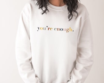 May include: White sweatshirt with the text "you're enough." in colorful letters.