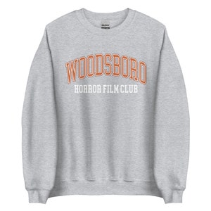 May include: Gray sweatshirt with the text "WOODSBORO HORROR FILM CLUB" in orange and white lettering.