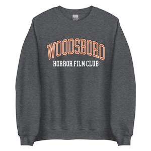 May include: Dark gray sweatshirt with the text "WOODSBORO HORROR FILM CLUB" in orange and white lettering.