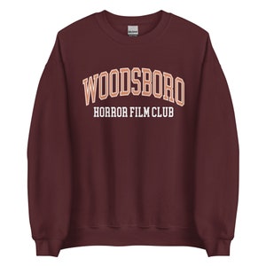 May include: Burgundy sweatshirt with the text "WOODSBORO HORROR FILM CLUB" in orange and white.