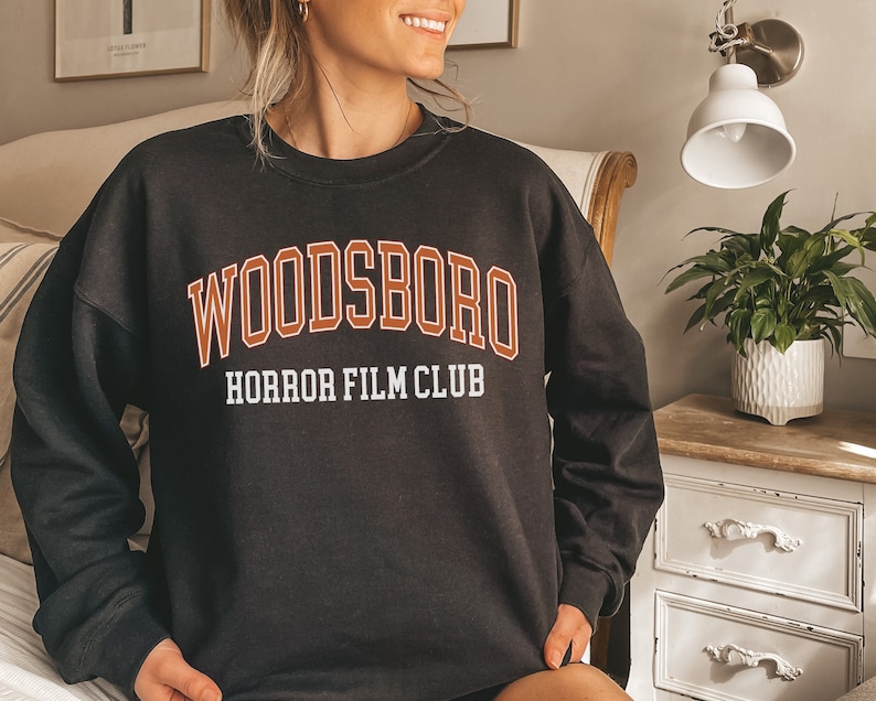 May include: Black sweatshirt with a white and orange graphic that says "Woodsboro Horror Film Club".