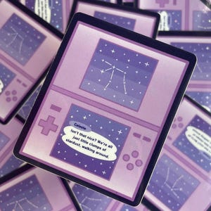 Puede incluir: Un montón de pegatinas moradas con un diseño de juego portátil retro. Cada pegatina tiene una pantalla que muestra una constelación y el texto "Celeste Isn't that nice? We're all just little clumps of stardust, walking around."