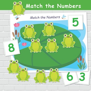以下が含まれることがあります： 「Match the Numbers」というタイトルの、スイレンの葉の上に漫画のカエルが描かれたカラフルな教育ゲーム。ゲームには数字カードとマッチングアクティビティが含まれています。背景には、ガマとトンボのある池のシーンがあります。
