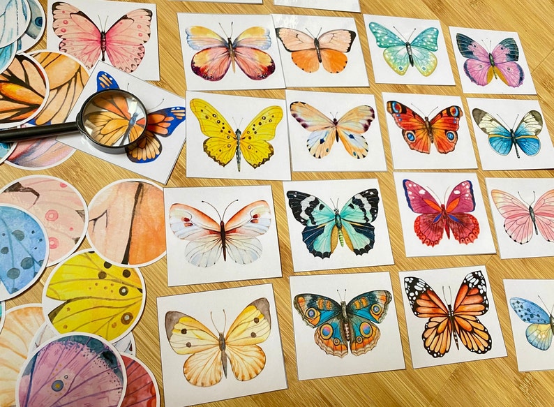 May include: A collection of colorful butterfly stickers on white cardstock. The butterflies are painted in various shades of pink, blue, green, yellow, and orange. The stickers are arranged in a grid pattern on a wooden surface.