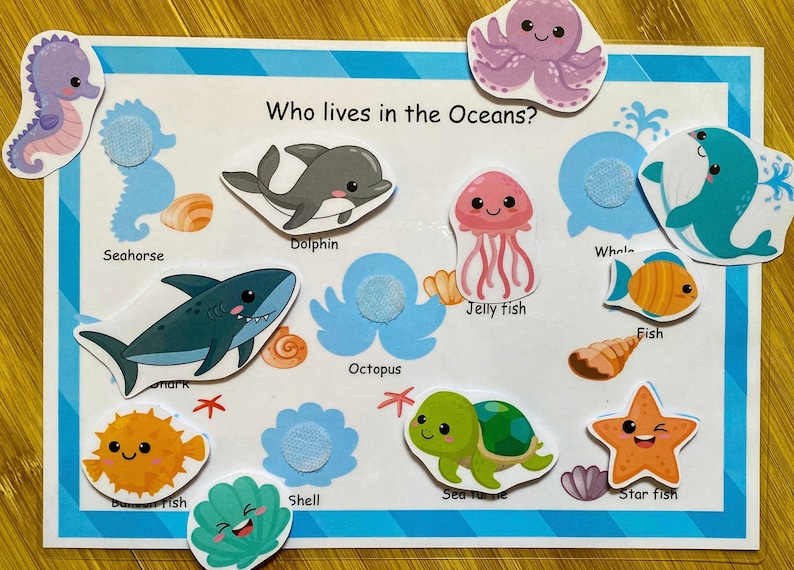 May include: A colorful educational board game for kids featuring various sea creatures like a seahorse, dolphin, whale, jellyfish, octopus, fish, sea turtle, and starfish. The board has a blue and white striped background with the text "Who lives in the Oceans?" at the top.