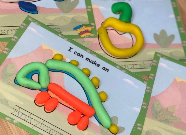 K&ouml;nnte beinhalten: Ein gr&uuml;ner und orangefarbener Play-Doh-Dinosaurier mit dem Text "Ich kann einen Ankylosaurus machen" auf einer wei&szlig;en Karte mit gr&uuml;nem Rand.