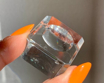 Puede incluir: Un soporte para anillos de vidrio transparente con una base cuadrada. El soporte está diseñado para exhibir un anillo.