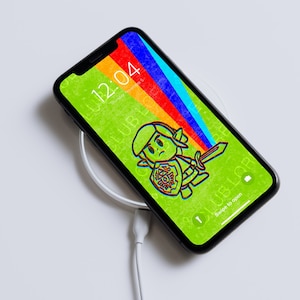 May include: A black iPhone with a green, rainbow, and blue background. The phone is on a white wireless charging pad with a white charging cable. The phone screen displays a cartoon character with a sword and shield. The time is 12:04.