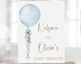 Puede incluir: Bienvenido a la fiesta de bienvenida al bebé de Olivia con un globo azul de acuarela y hojas verdes de eucalipto. El cartel está en un caballete de madera.