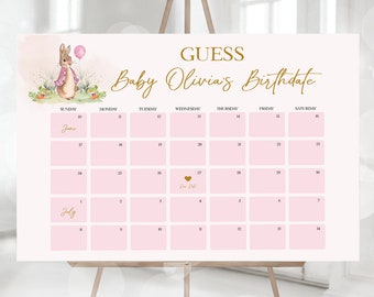 May include: A pink and white calendar with the text "Guess Baby Olivia's Birthdate" in gold lettering. The calendar has the months of June and July with the days of the week labeled. A small heart with the text "Due Date" is in the center of the calendar.