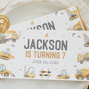 May include: A white chocolate bar wrapper with a construction theme. It features a yellow excavator, a cement mixer, and a crane. The text on the wrapper reads "Jackson is turning 7" and "June 25, 20XX".