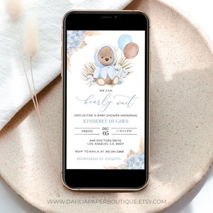 Pu&ograve; includere: Un invito a una festa di baby shower blu e marrone con un orsacchiotto che indossa un maglione con cappuccio blu e tiene dei palloncini. Il testo recita "We can barely wait" e include la data, l'ora e il luogo dell'evento. Sono incluse anche le informazioni RSVP.