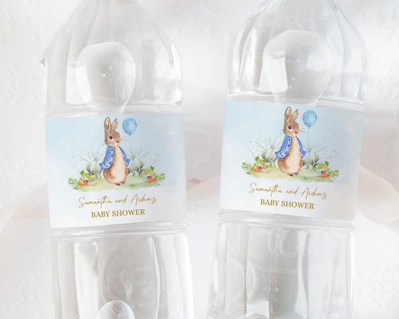 May include: Two clear plastic water bottles with blue and white labels featuring a watercolour illustration of Peter Rabbit holding a blue balloon. The labels also include the text "Samantha and Aiden's Baby Shower".