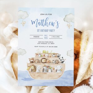 K&ouml;nnte beinhalten: Eine blaue und wei&szlig;e Einladung mit einer Aquarell-Illustration einer h&ouml;lzernen Arche, die mit Tieren gef&uuml;llt ist. Der Text lautet "Join us for Matthew's 1st Birthday Party, Friday, Dec 05, 2 to 5 PM, 3145 Doctors Drive, Los Angeles, CA, 90017, RSVP to Kayla at 310-341-3368."