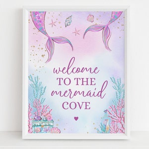 May include: A printable sign with a mermaid tail design in shades of purple and blue. The sign says "Welcome to the Mermaid Cove" with a small heart below the text.