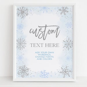 May include: A framed print with a winter theme. The artwork features a light blue watercolor background with silver and light blue snowflakes. The text "custom TEXT HERE" is displayed in silver glitter, with additional text below.
