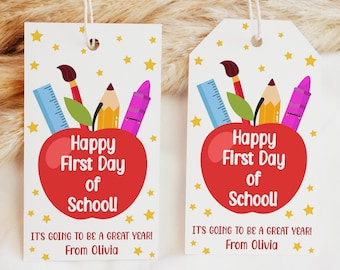 Puede incluir: Dos etiquetas de regalo en forma de manzana roja con fondo blanco y estrellas doradas. Las etiquetas tienen el texto "Happy First Day of School" y "It's going to be a great year! From Olivia".