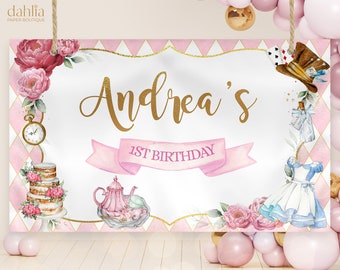 May include: A white and pink Alice in Wonderland themed birthday banner with gold lettering. The banner says "Andrea's 1st Birthday".