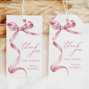 Pode incluir: Duas etiquetas brancas de agradecimento com um laço de fita rosa aquarela. O texto nas etiquetas diz "Obrigado por vir com amor, Audrey".