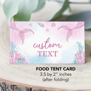 May include: Pink and blue mermaid-themed food tent card with a mermaid tail on each side, seashells, and stars. The text "custom TEXT" is in the center of the card. The card measures 3.5 by 2 inches when folded.