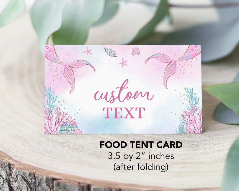 May include: Pink and blue mermaid-themed food tent card with a mermaid tail on each side, seashells, and stars. The text "custom TEXT" is in the center of the card. The card measures 3.5 by 2 inches when folded.