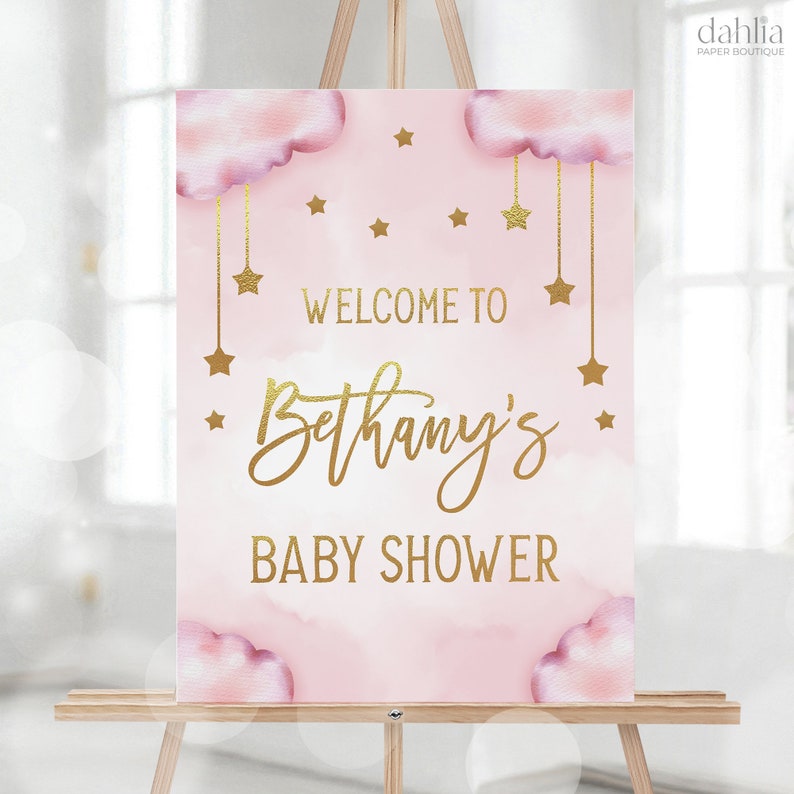 Może przedstawiać: R&oacute;żowo-złoty napis powitalny na baby shower z chmurami i gwiazdami. Napis brzmi "Witamy na baby shower Bethany".