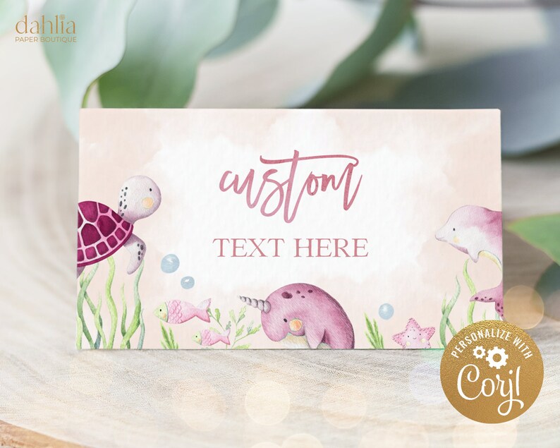 May include: Pink and white printable place card with a watercolor illustration of a sea turtle, a narwhal, a dolphin, and starfish. The text "custom text here" is written in pink on the card.