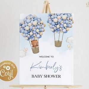 K&ouml;nnte beinhalten: Willkommen zur Babyparty von Kimberly Schild mit einem blauen und beigefarbenen Ballon-Hei&szlig;luftballon mit einem Teddyb&auml;ren im Korb. Das Schild steht auf einem Holzst&auml;nder.