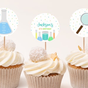 May include: Three cupcake toppers with a science theme. The toppers feature a beaker, a magnifying glass, and a beaker with the text "Jackson's 8th Birthday".