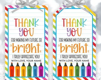 Op de afbeelding: Twee printbare cadeaulabels met een regenboogkleurige gestreepte achtergrond. De labels bevatten de tekst "Bedankt voor het maken van mijn toekomst zo helder. Ik waardeer je echt! Met liefde, jouw naam." en een rij kleurrijke stiften.