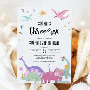 May include: A white birthday invitation with a dinosaur theme. The invitation says "Sophia is three-rex" and includes details about the party, including the date, time, and location. The invitation is decorated with colorful dinosaurs, stars, and a sun.