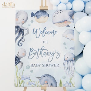 May include: A blue and white baby shower welcome sign with a watercolor illustration of sea creatures, including an octopus, a whale, a turtle, a jellyfish, a narwhal, and fish. The sign reads "Welcome to Bethany's Baby Shower".