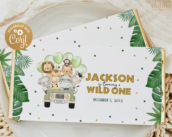 May include: A white and gold personalized chocolate bar wrapper with a jungle theme. The wrapper features a cartoon jeep with animals, green leaves, and gold confetti. The text on the wrapper reads "JACKSON is turning a WILD ONE DECEMBER 5, 20XX".