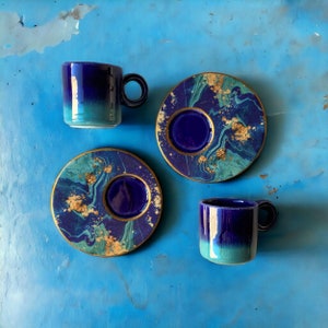 Puede incluir: Tres tazas de caf&eacute; y platillos azules y dorados. Las tazas y los platillos tienen un dise&ntilde;o marmoleado con remolinos azules, dorados y blancos.