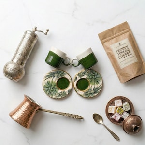 May include: An assortment of Turkish coffee items, including two green and white coffee cups, matching saucers with a succulent design, a copper coffee pot, a coffee grinder, a bag of coffee, and a small dish of Turkish delight.