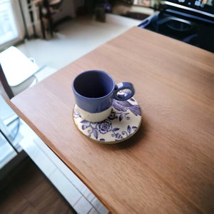 May include: A blue and white ceramic coffee cup and saucer with a floral design. The cup is sitting on a wooden table.