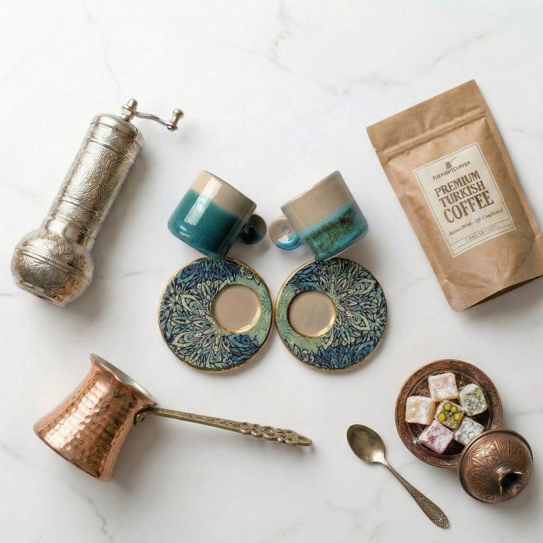May include: An assortment of Turkish coffee items, including two small blue and beige mugs with matching saucers, a copper coffee pot, a silver coffee grinder, a bag of coffee, and a small dish of Turkish delight.