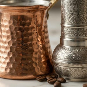 Extreme close-up showing the high-quality handmade textures: irregular hammer marks on a copper cezve pot and intricate traditional engravings on a silver coffee grinder.