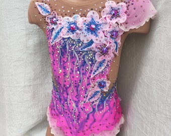 May include: A pink and purple leotard with a floral design. The leotard features a sheer neckline and sleeves, with a gradient effect from pink to purple. The floral design includes white and blue flowers with crystal embellishments.