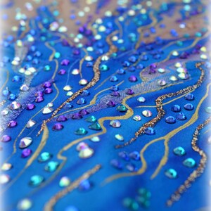 May include: A close-up of a blue fabric with gold and silver glitter and rhinestones. The rhinestones are in various shapes and sizes and are arranged in a pattern.