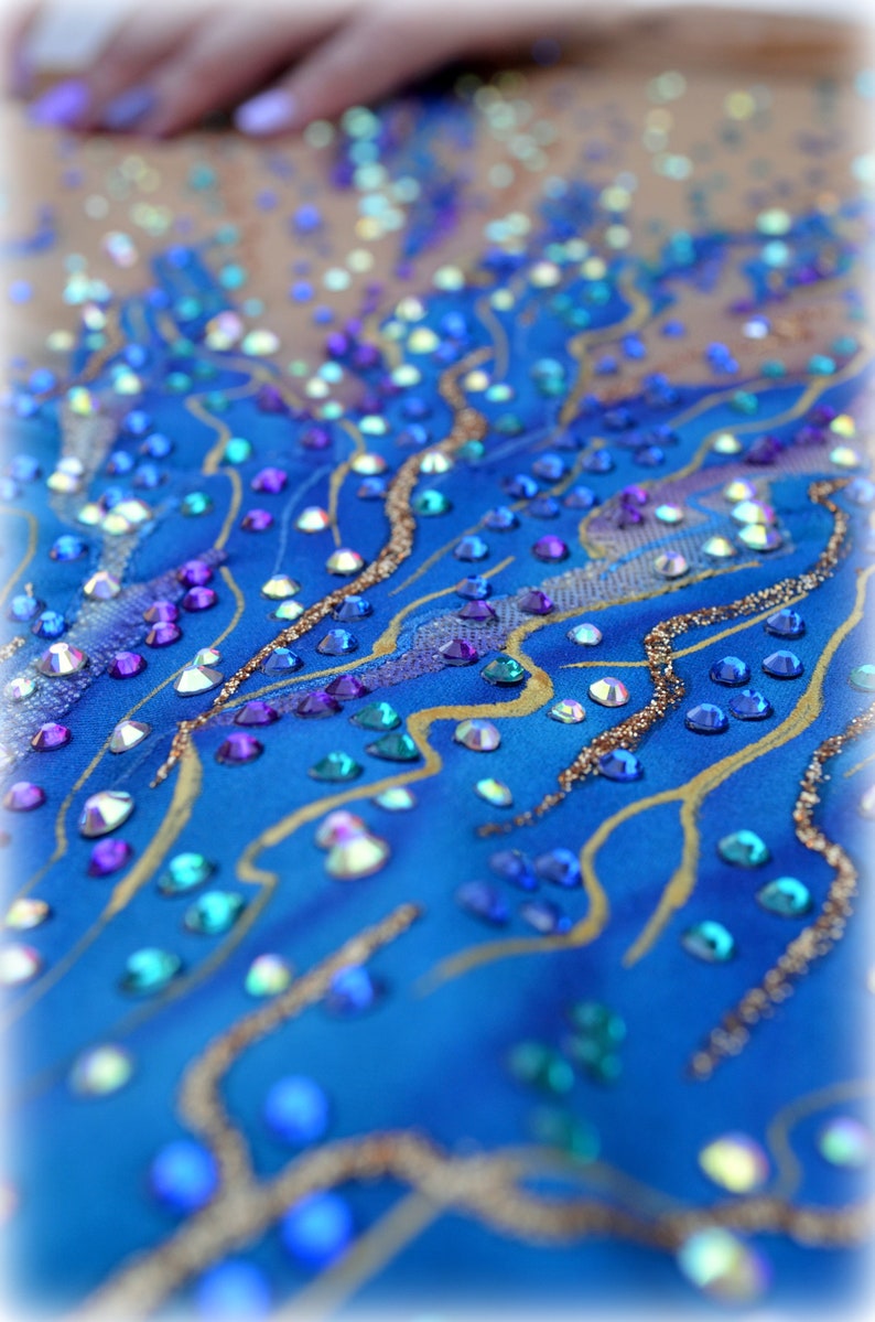 May include: A close-up of a blue fabric with gold and silver glitter and rhinestones. The rhinestones are in various shapes and sizes and are arranged in a pattern.